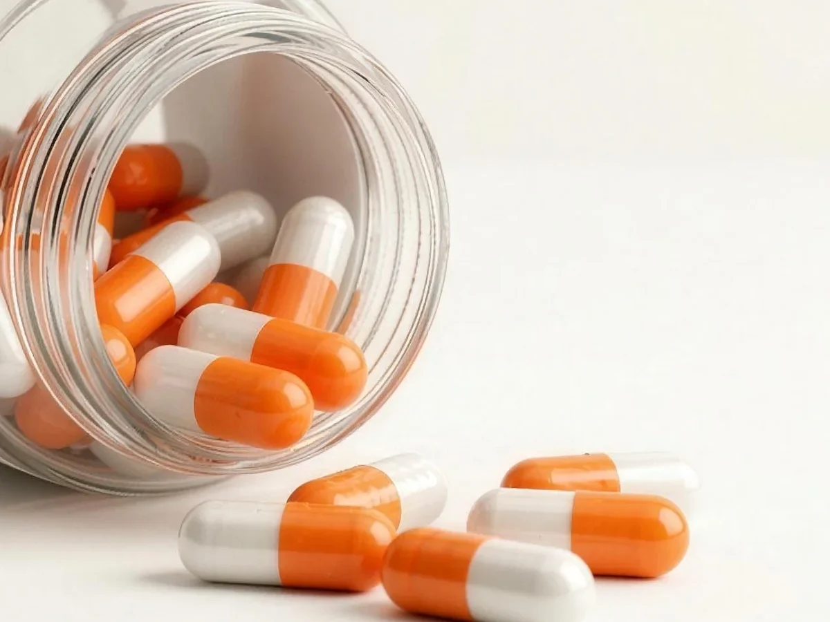 Close up of orange and white capsules spilling from a glass jar.